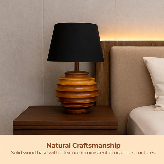 Wooden lamp with black shade on a nightstand next to a bed, with 'Natural Craftsmanship' text.