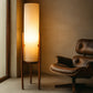 Tall floor lamp with a soft glow next to a brown leather chair in a room with beige walls.