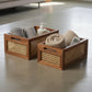 Two wooden baskets with rattan sides containing towels and a bottle on a light-colored floor.